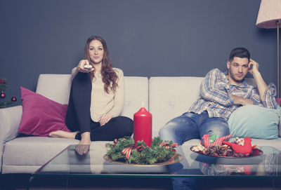 Man and woman sitting on sofa while watching tv during christmas