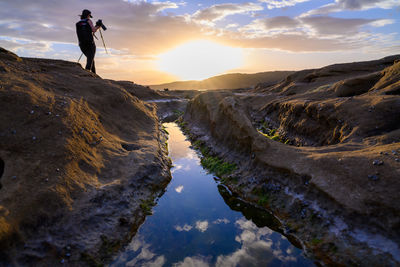 Man standing on rock against sky during sunset