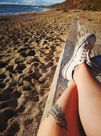 Low section of woman relaxing on sand at beach