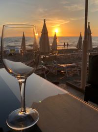 Wine glass on table by sea against sky during sunset