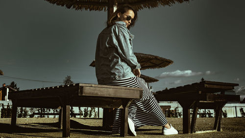 Side view of woman sitting on chair against sky