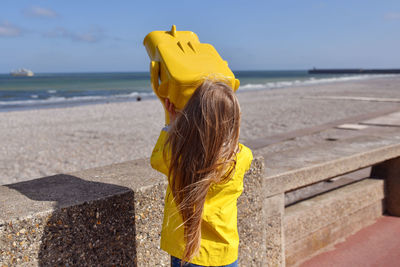 Rear view of woman standing on retaining wall against sea