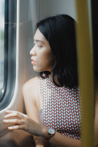 Close-up of young woman looking through window while traveling in train