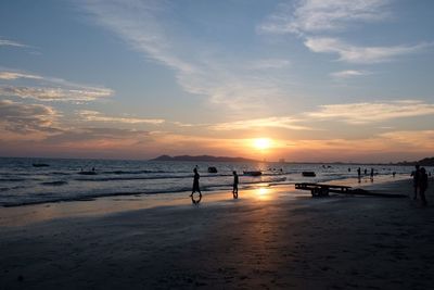 Silhouette people standing on beach against sky during sunset