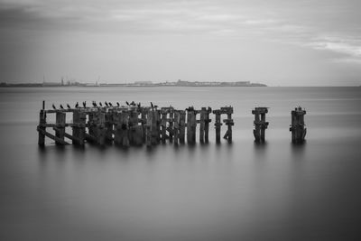 Wooden posts in sea against sky