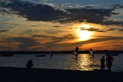Silhouette people on beach against sky during sunset