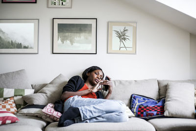 Full length of woman using mobile phone while lying on sofa at home