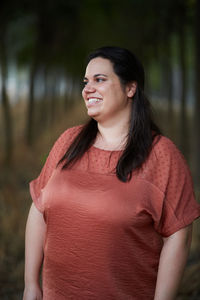 Cheerful young chubby female in casual apparel looking away with toothy smile in daylight