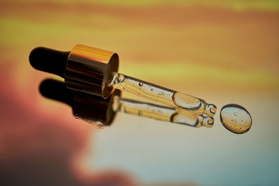 A pipette with facial serum against a sunset background in bright orange tones.