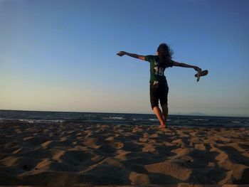 Rear view of woman with arms outstretched standing at beach during sunset