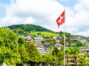 Red flag amidst trees and buildings against sky in city