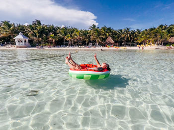 Young woman floating on inflatable ring in sea against blue sky