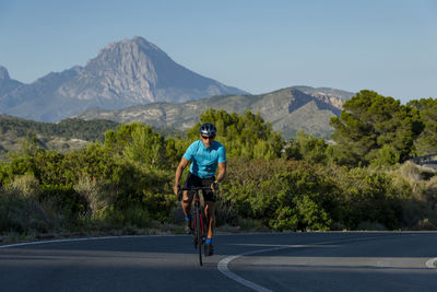A man, standing up on his pedals, bikes uphill in alicante road