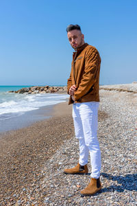 Full length of young man standing on beach against clear sky