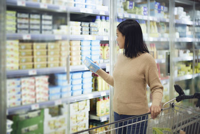 Woman in supermarket standing in front of fridge and choosing food