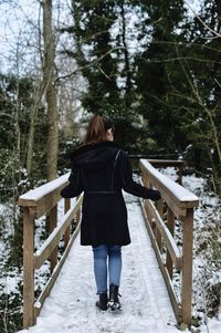 Rear view of young woman standing snow covered footbridge