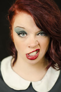 Portrait of young woman snarling against black background