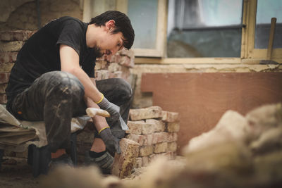 A young man cleans bricks with an axe.