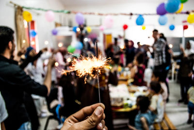 Cropped hand of person holding illuminated sparkler in party