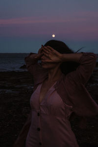 Woman standing on beach against sky during sunset