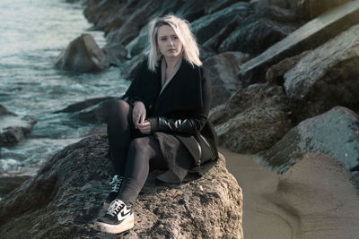 Portrait of a woman sitting on rock by sea