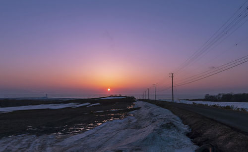 Snow covered landscape against sky during sunset