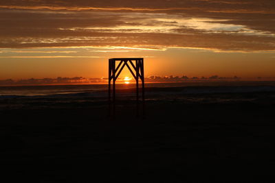 Silhouette lifeguard hut on beach against sky during sunset