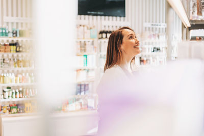 Adult pretty smiling woman with dark hair in cosmetics and perfume store, holiday shopping