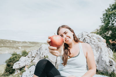 Young woman holding apple against sky