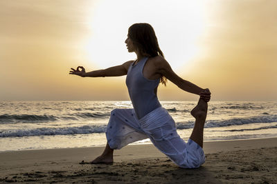 Attractive young woman practices yoga by the sea at sunset. eka pada rajakapotasana yoga pose.
