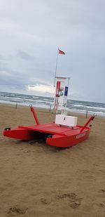 Red ship moored on beach against sky