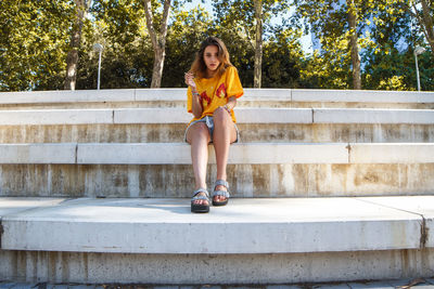 Full length of young woman sitting on steps against trees