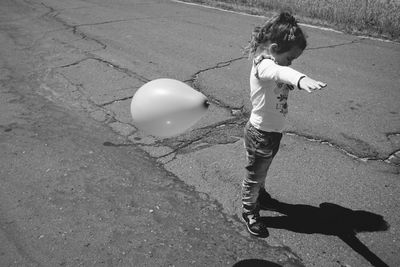 Full length side view of girl standing by helium balloon in mid-air on road