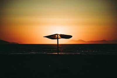Silhouette lifeguard hut on beach against sky during sunset
