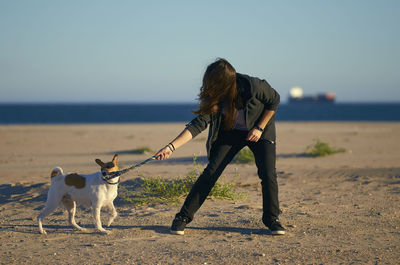 Woman playing with dog at beach against blue sky