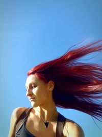 Low angle view of woman looking away against blue sky