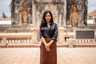 Portrait of young woman standing against built structure