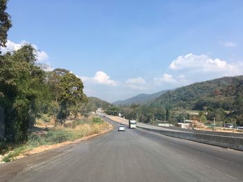 Road by trees against sky