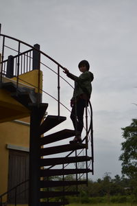 Low angle view of woman standing on spiral staircase against sky