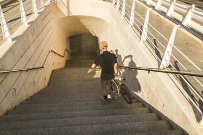 High angle view of young man with bicycle moving down on steps in building