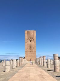 People walking towards historical building against clear blue sky