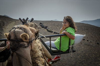 Side view of girl riding on camel at desert against clear sky