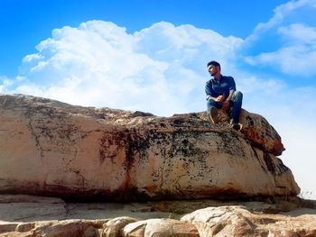 Low angle view of man sitting on rock formation against sky