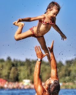 Cropped image of man catching daughter against sky
