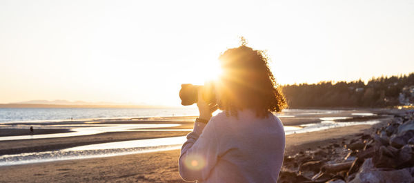 Woman standing on beach against sky during sunset