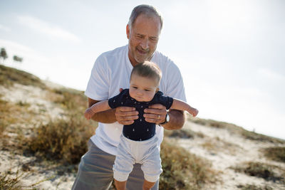 Grandfather playing & holding grandson while standing on beach