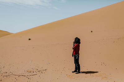 Full length of man photographing while standing on sand in desert against sky