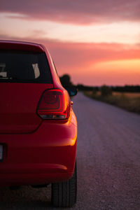 Close-up of red car on road against sky during sunset