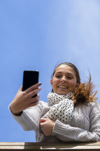 Portrait of woman holding mobile phone against sky