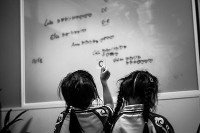 Rear view of girls standing in front of glass blackboard